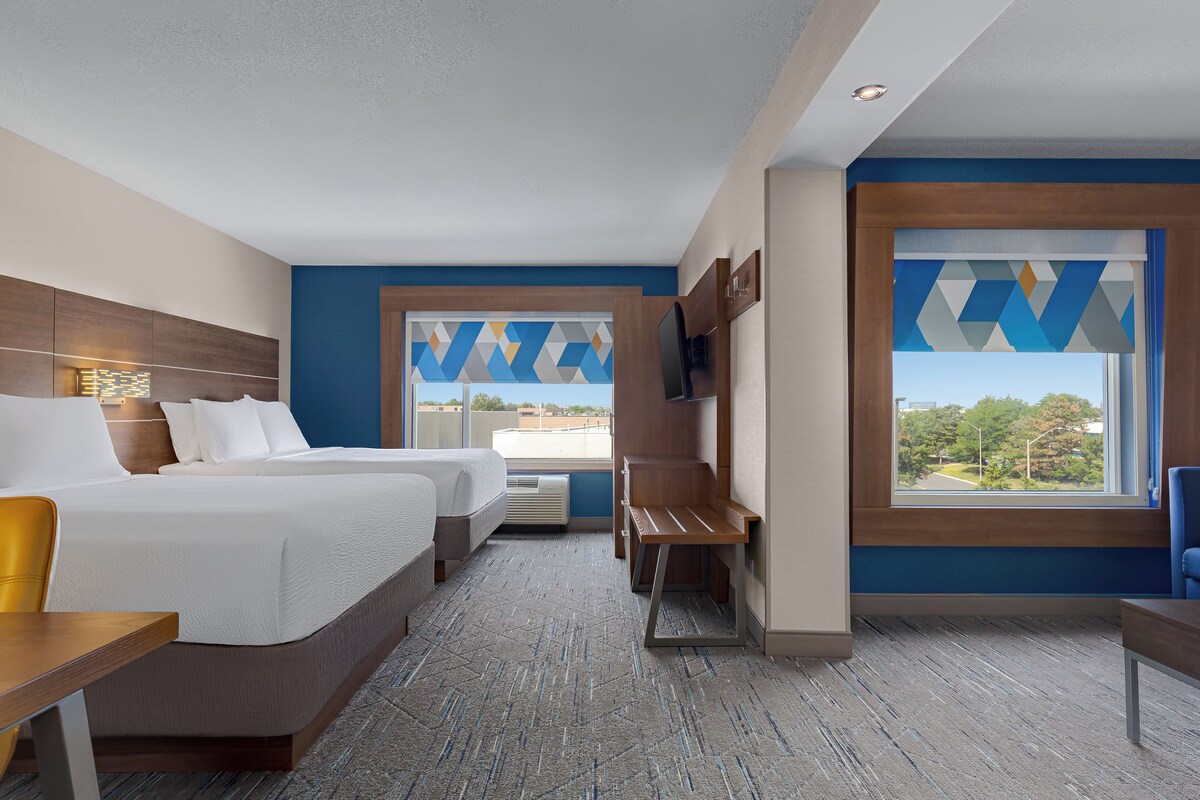 A hotel room with two beds, a desk, a TV, and a large window with a view.