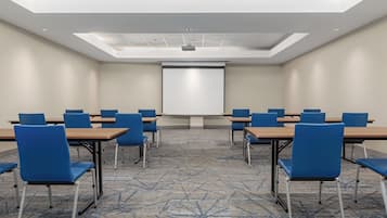Une salle de conférence équipée d’un écran de projection, de chaises bleues et d’un sol recouvert de moquette.