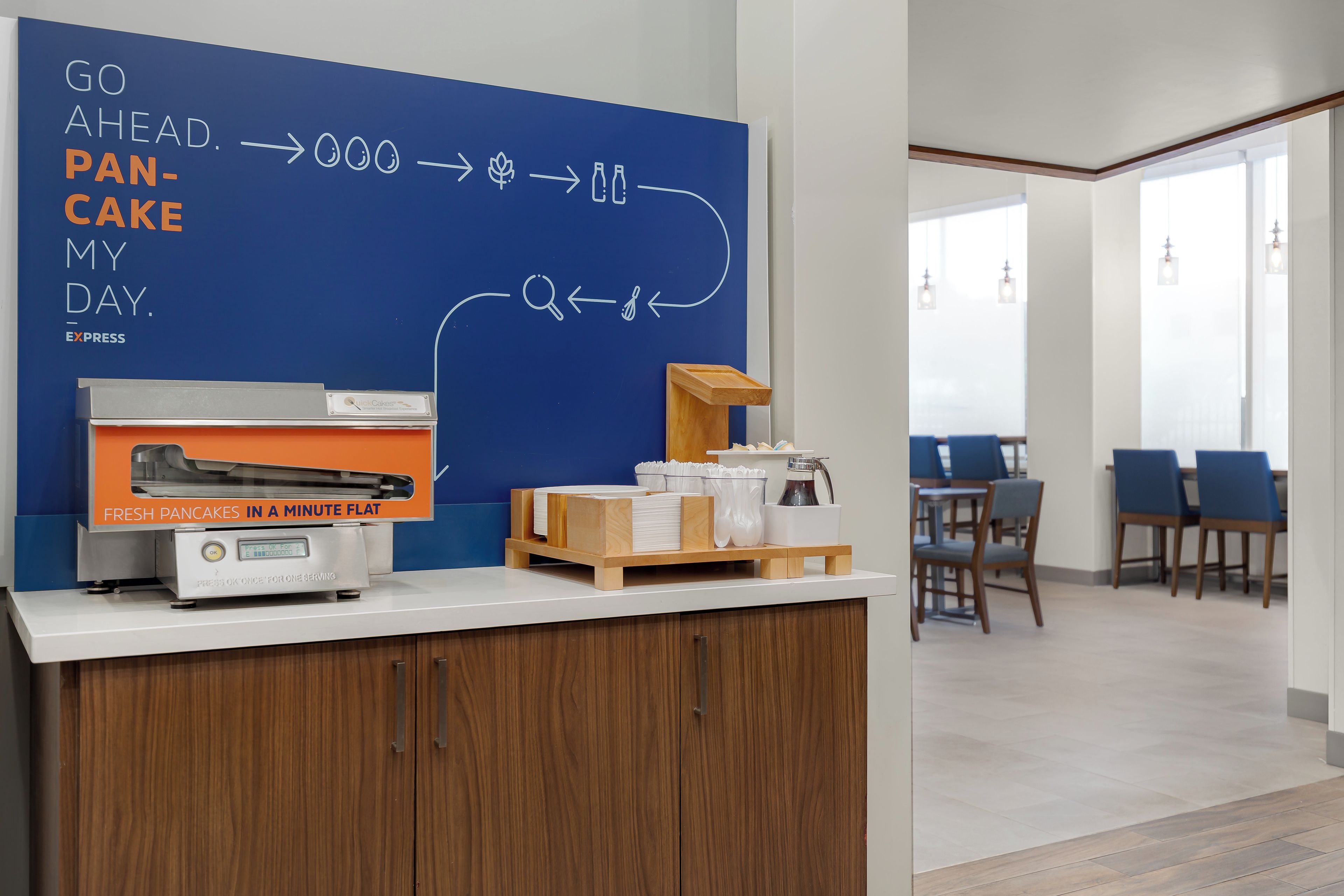 A breakfast area with a blue wall displaying a breakfast menu, a pancake maker, and a coffee station.