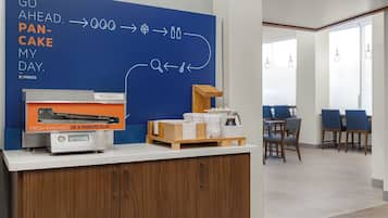 A breakfast area with a blue wall displaying a breakfast menu, a pancake maker, and a coffee station.