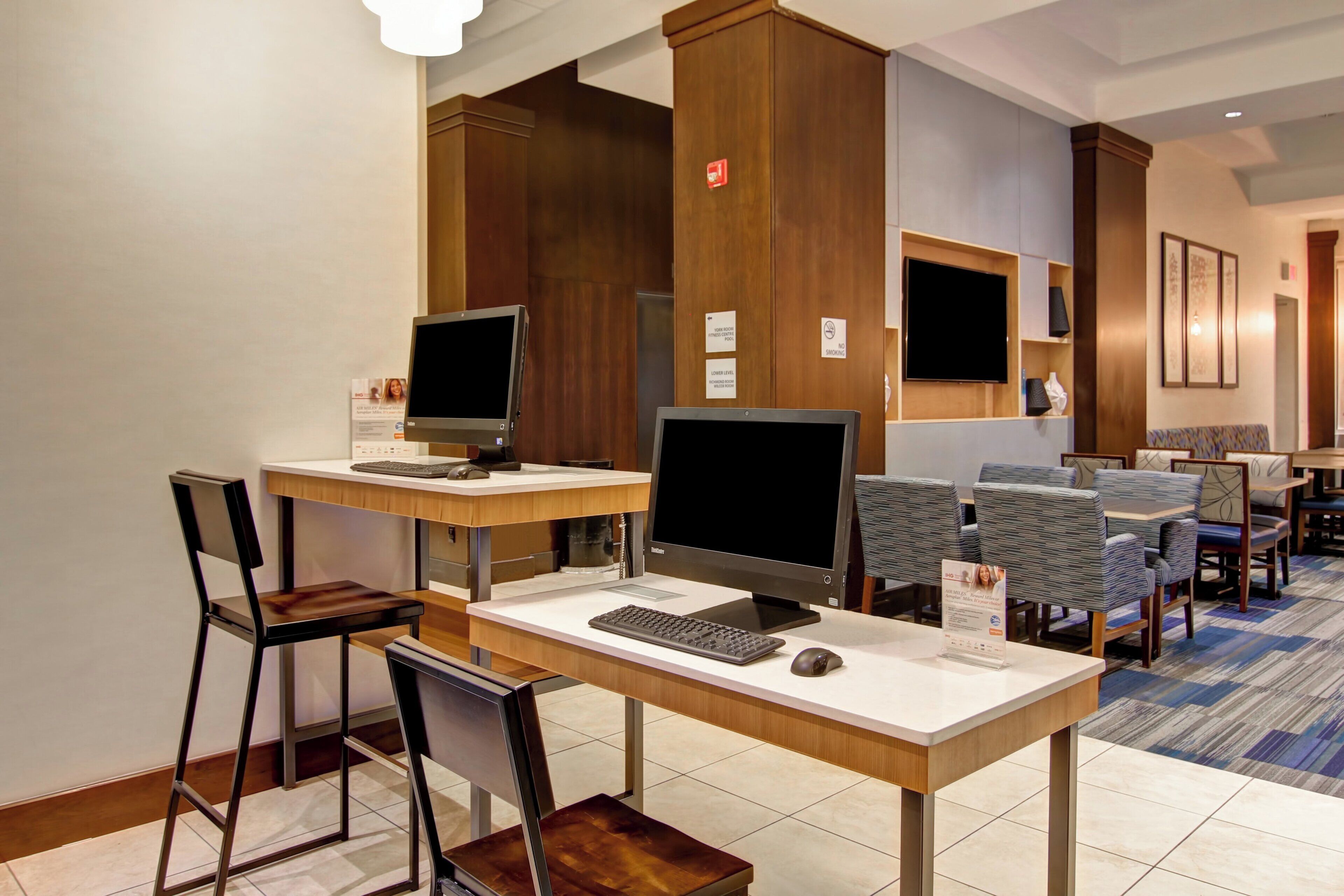 Un hall de hotel con mostrador de recepción, computadoras, zona de estar y una pantalla de televisión.