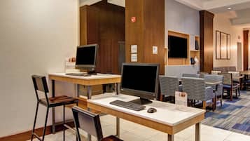 Un hall de hotel con mostrador de recepción, computadoras, zona de estar y una pantalla de televisión.
