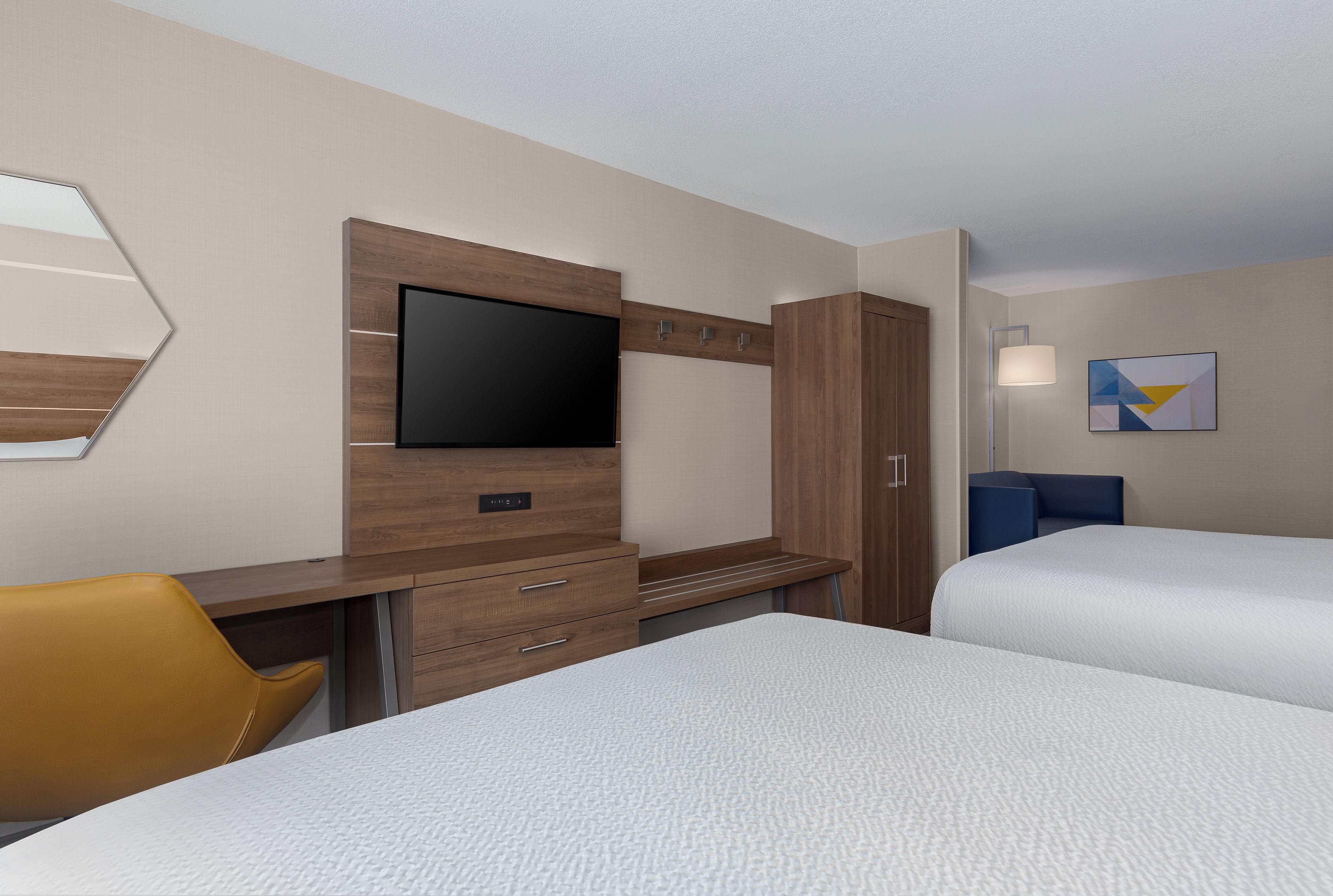 A hotel room with a bed, a desk with a flat-screen TV, a wardrobe, a chair, and a bedside table.