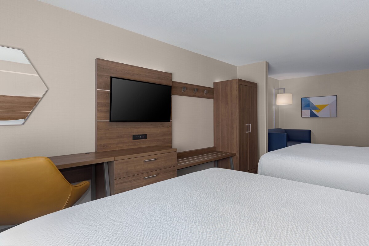 A hotel room with a bed, a desk with a flat-screen TV, a wardrobe, a chair, and a bedside table.