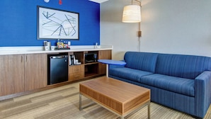 A modern living room with a blue sofa, a wooden coffee table, a microwave, and a sink in a compact kitchenette.