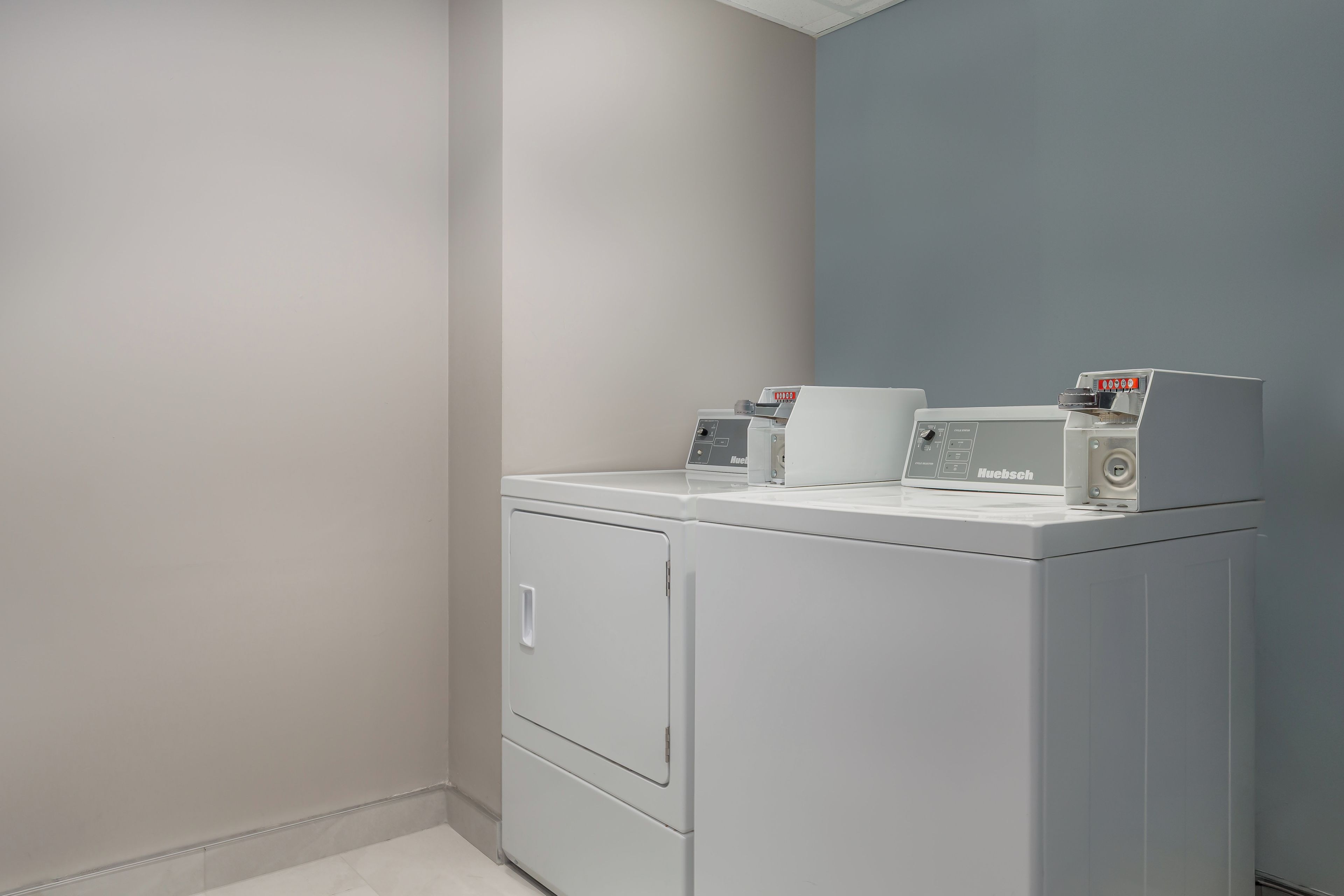 A laundry room with a front-loading washer and dryer, a control panel, and a wall-mounted drying rack.