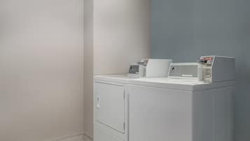 A laundry room with a front-loading washer and dryer, a control panel, and a wall-mounted drying rack.