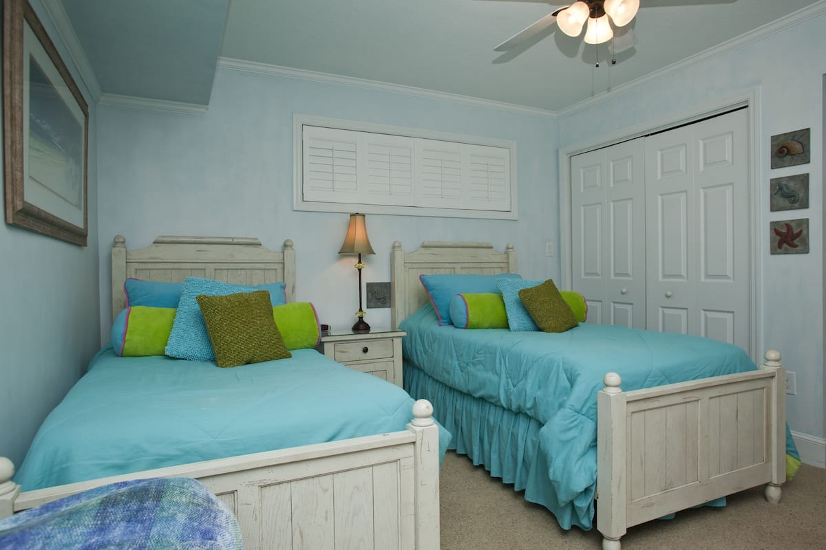 A bedroom with two beds, a ceiling fan, a nightstand, and a door.