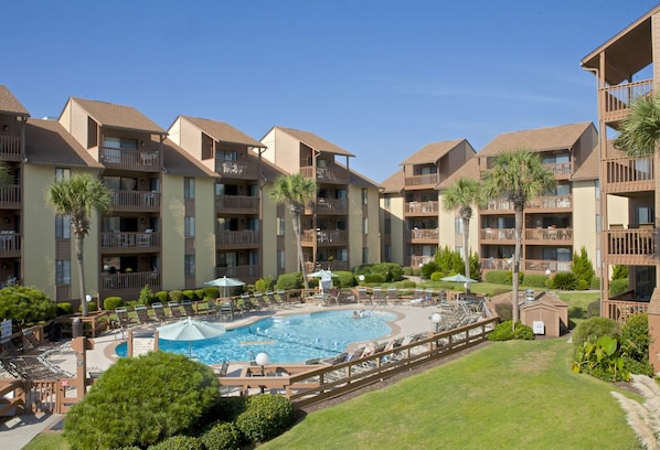 A hotel with multiple balconies, a swimming pool, and well-maintained lawns.