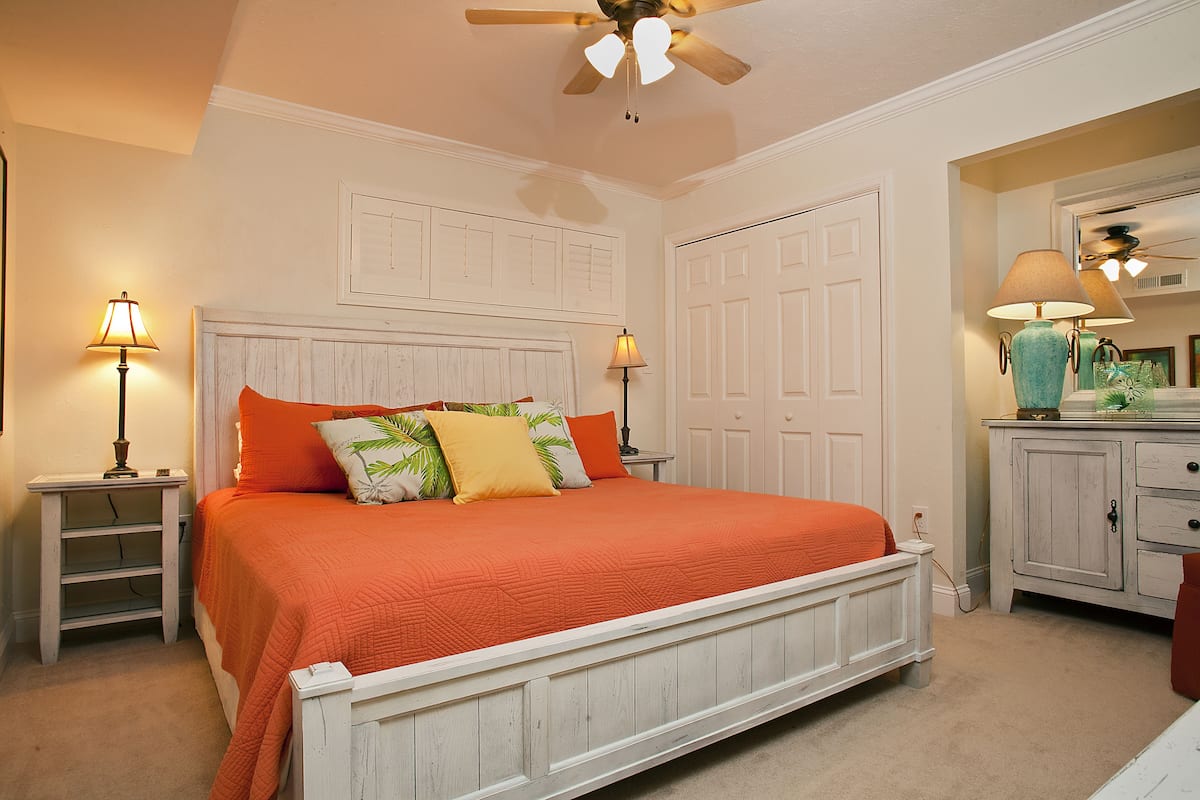 A bedroom with a bed, two bedside tables, a nightstand, a ceiling fan, and a dresser with a mirror.