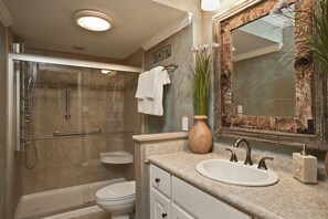 A bathroom with a glass-enclosed shower, a toilet, a sink with a mirror, and a vase with flowers.