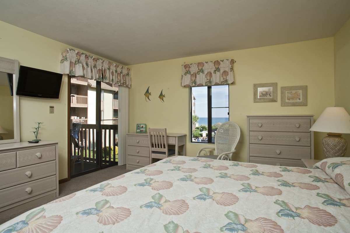 A bedroom with a bed, dresser, chair, and a television on the wall.