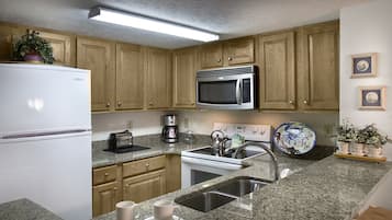 A kitchen with wooden cabinets, a stainless steel microwave, a white refrigerator, a granite countertop, a sink, and a coffee maker.