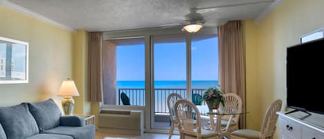 A room with a balcony, a sofa, a dining table with chairs, a TV, and a lamp.