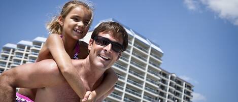 A man carrying a child on his back with a modern building in the background.