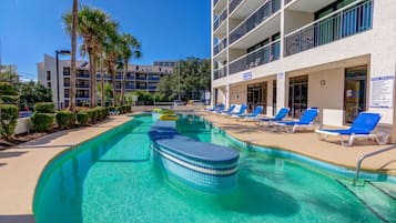 A swimming pool with blue lounge chairs and a building with balconies.