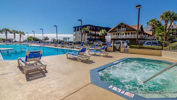 A swimming pool area with lounge chairs and a hot tub, surrounded by buildings and palm trees.