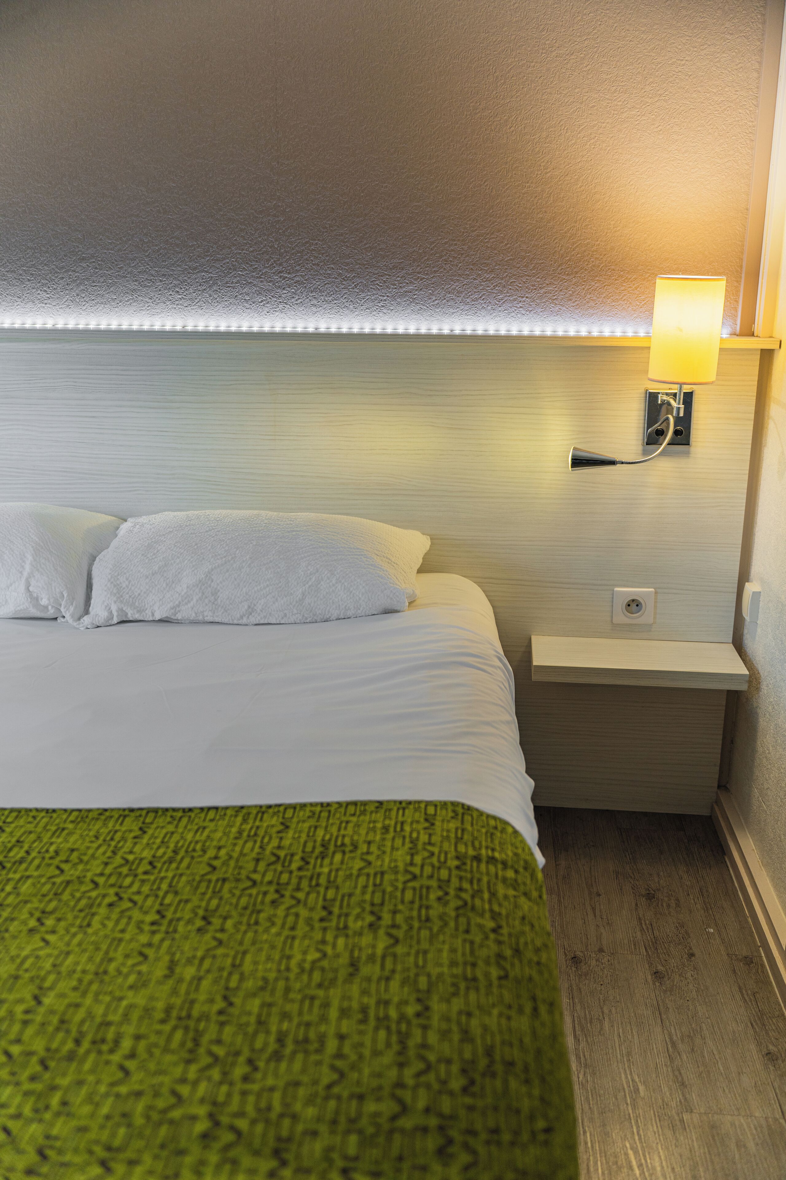 A hotel room with a neatly made bed, a bedside lamp, and a small nightstand.