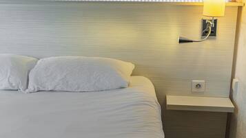 A hotel room with a neatly made bed, a bedside lamp, and a small nightstand.