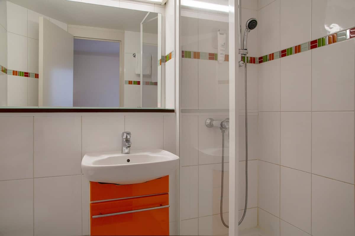 Un baño con un lavamanos blanco, un armario naranja, una ducha y un espejo.