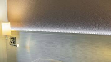 Ein ordentlich gemachtes Bett mit weißen Leinentüchern und einer grünen Tagesdecke, eine Wandlampe sowie eine strukturierte Wand.