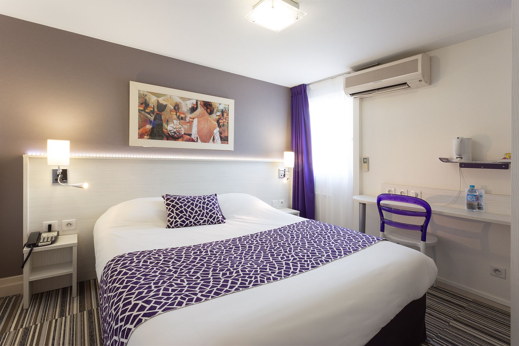 Hotelkamer met een bed, nachtkastje, stoel, bureau, airconditioning, schilderij en een badkamer met douchegordijn.