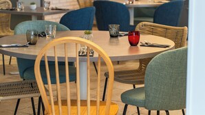 A dining area with round tables, chairs, and a kitchen in the background.