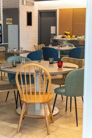 Een eetgedeelte met ronde tafels, stoelen en een keuken op de achtergrond.