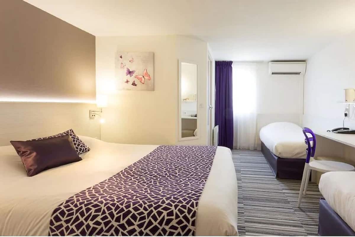 Una habitación de hotel con cama, escritorio, silla, espejo y puerta de baño.