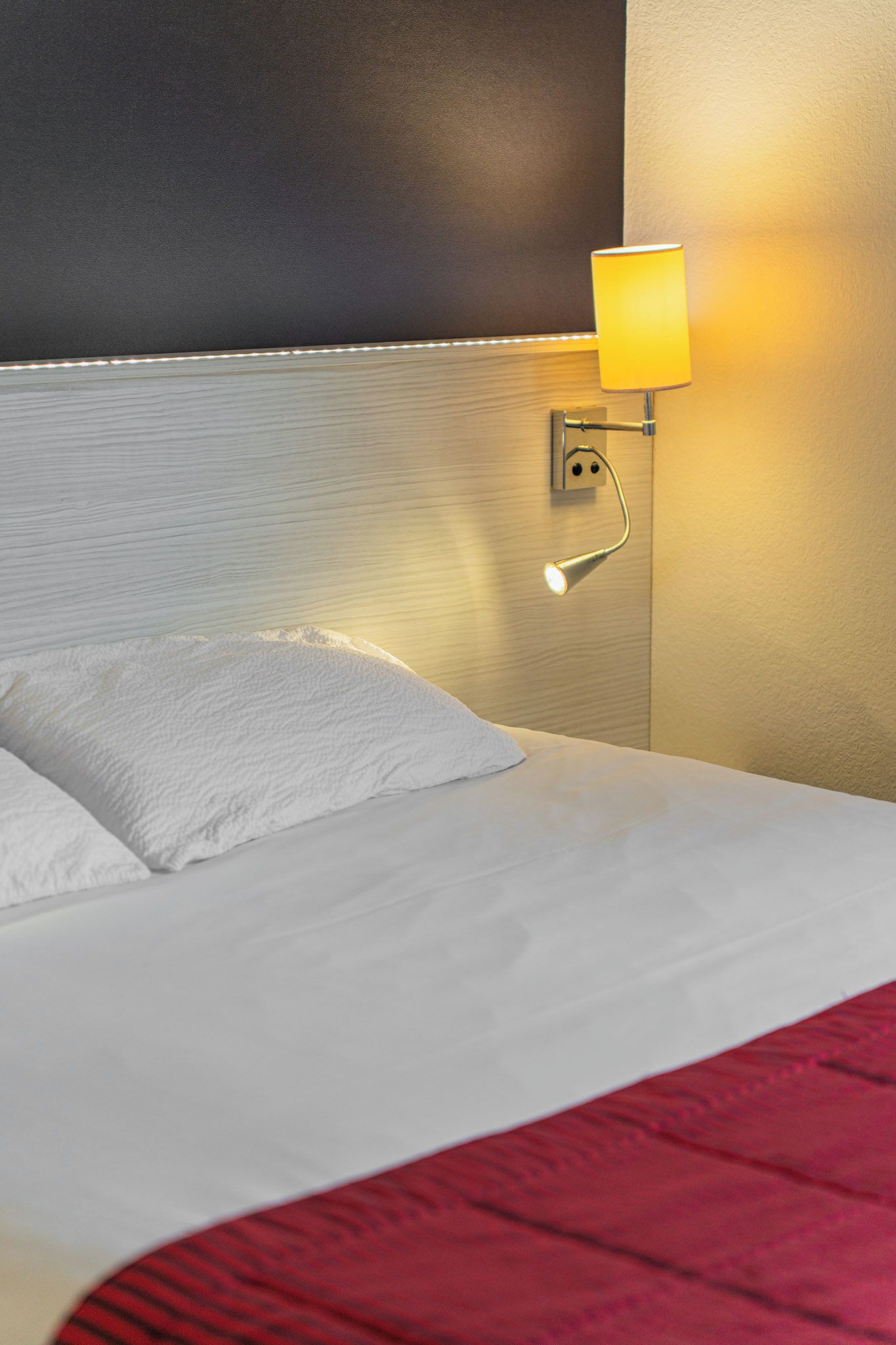 Ein Hotelzimmer mit Bett, einer Wandlampe und einer roten Decke.