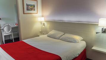 A hotel room with a bed, a desk, a chair, and a wall-mounted lamp.