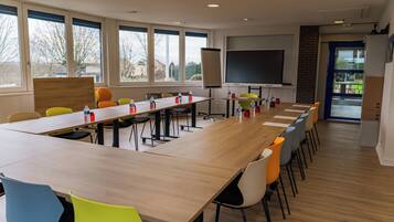 Een vergaderzaal met een lange tafel, meerdere stoelen, een projectiescherm en grote ramen.