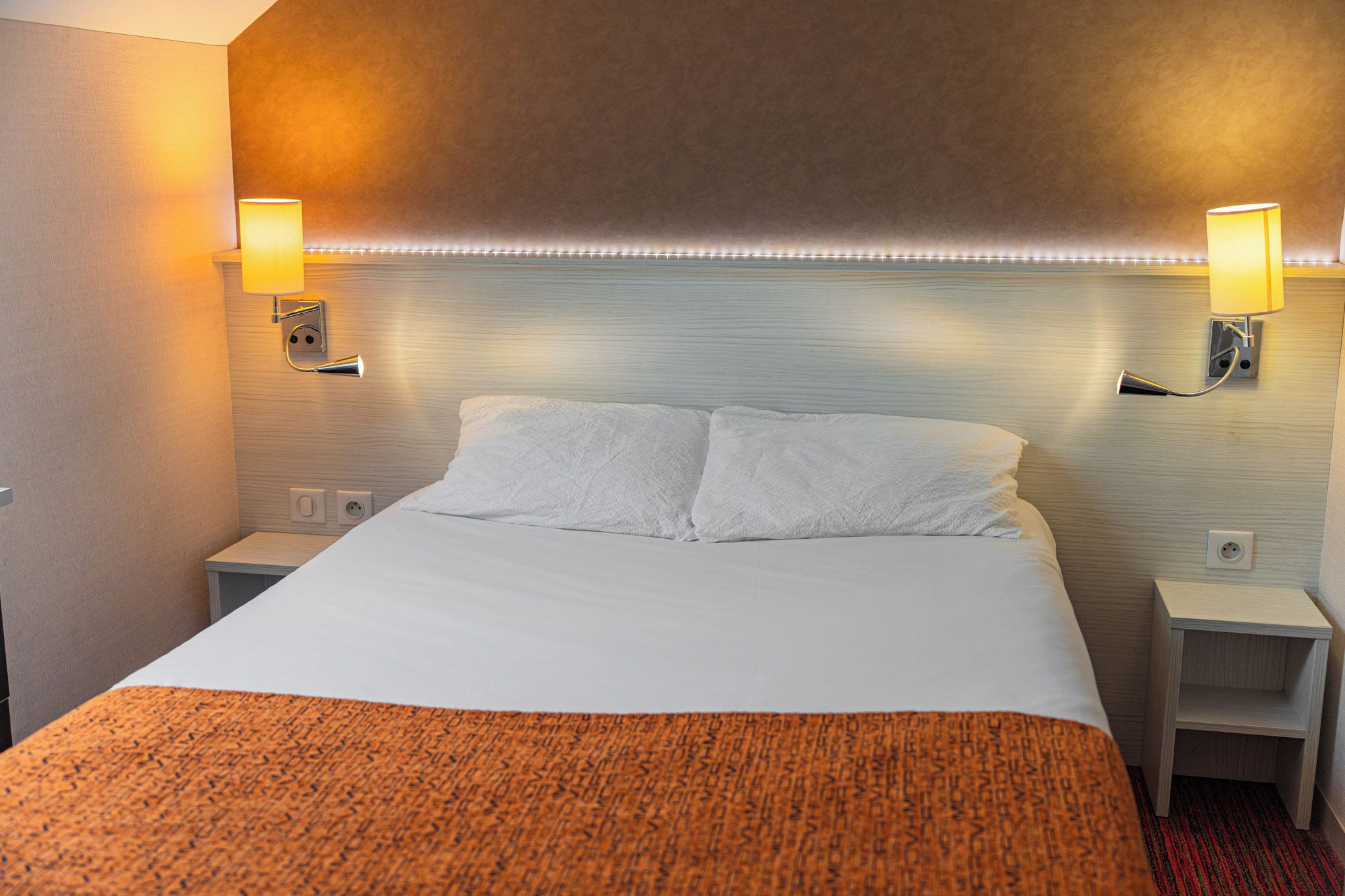 A hotel room with a large bed, two bedside tables, and wall-mounted lamps.