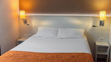 A hotel room with a large bed, two bedside tables, and wall-mounted lamps.