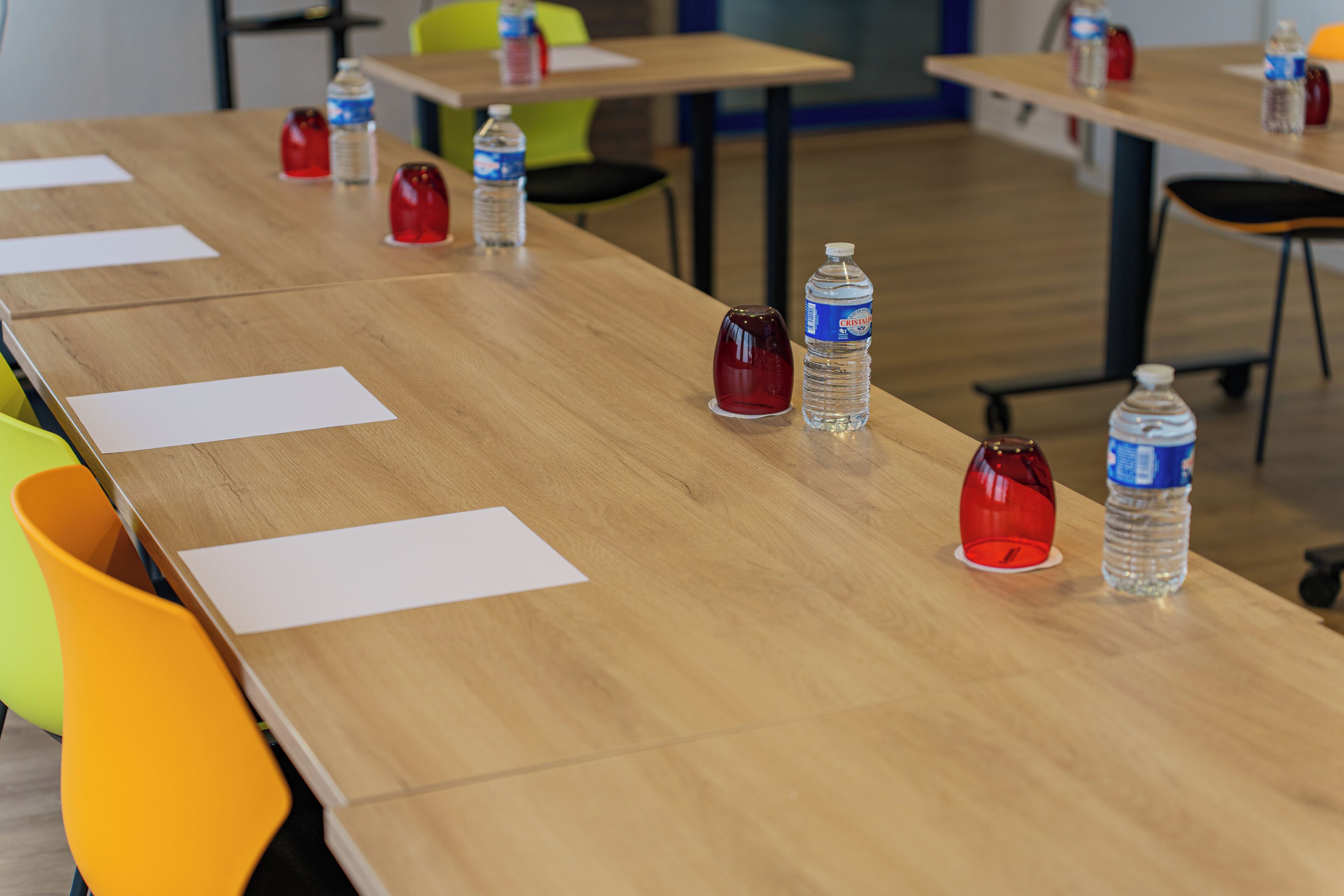 A conference room with long tables, chairs, and water bottles on each table.