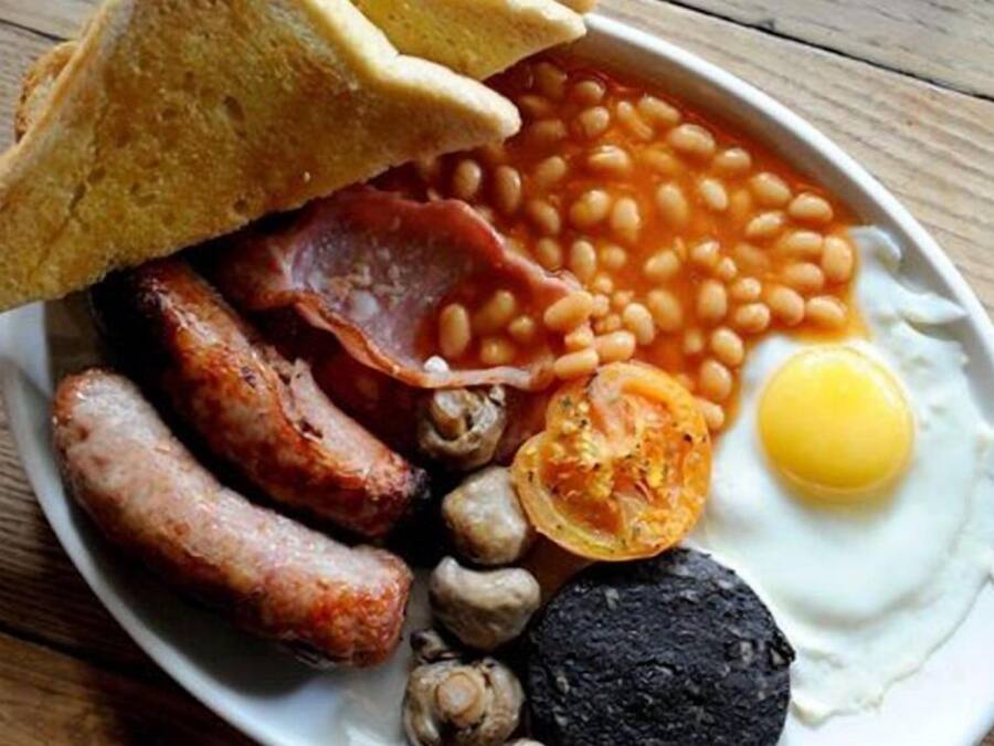 Ein Teller mit Frühstücksessen, darunter Toast, Bohnen, Würstchen, ein Spiegelei und Pilze.