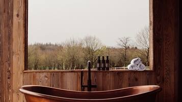 A copper bathtub in a wooden room with a window overlooking a forest.