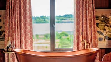 Relax in a spacious room with a bathtub overlooking a serene body of water and lush greenery.