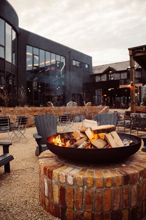 An outdoor seating area with a fire pit, brick seating, and a modern building in the background. - Glasson LakeHouse (Athlone)