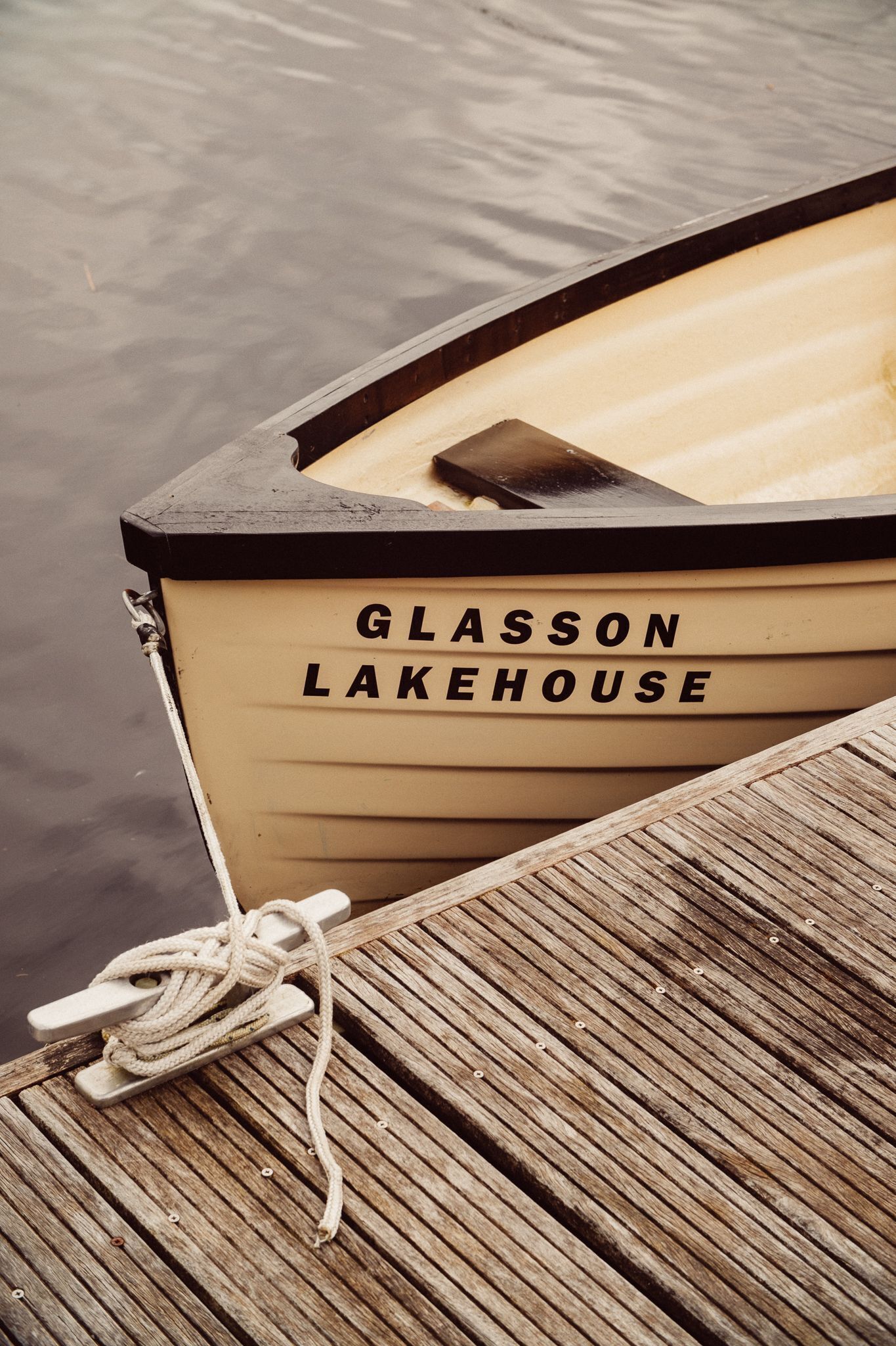 A wooden boat with the name "Glasson Lakehouse" on its side, docked at a wooden pier.