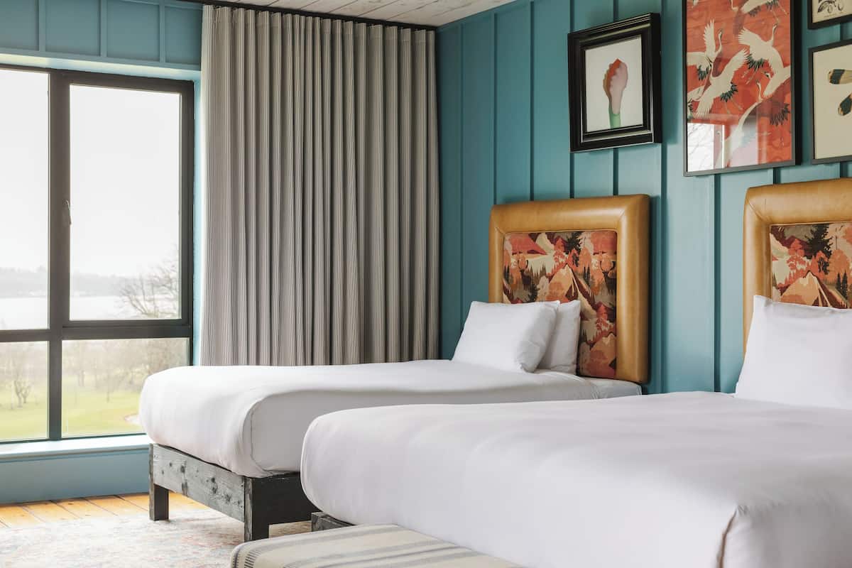 A hotel room with two beds, a large window, and artwork on the walls.