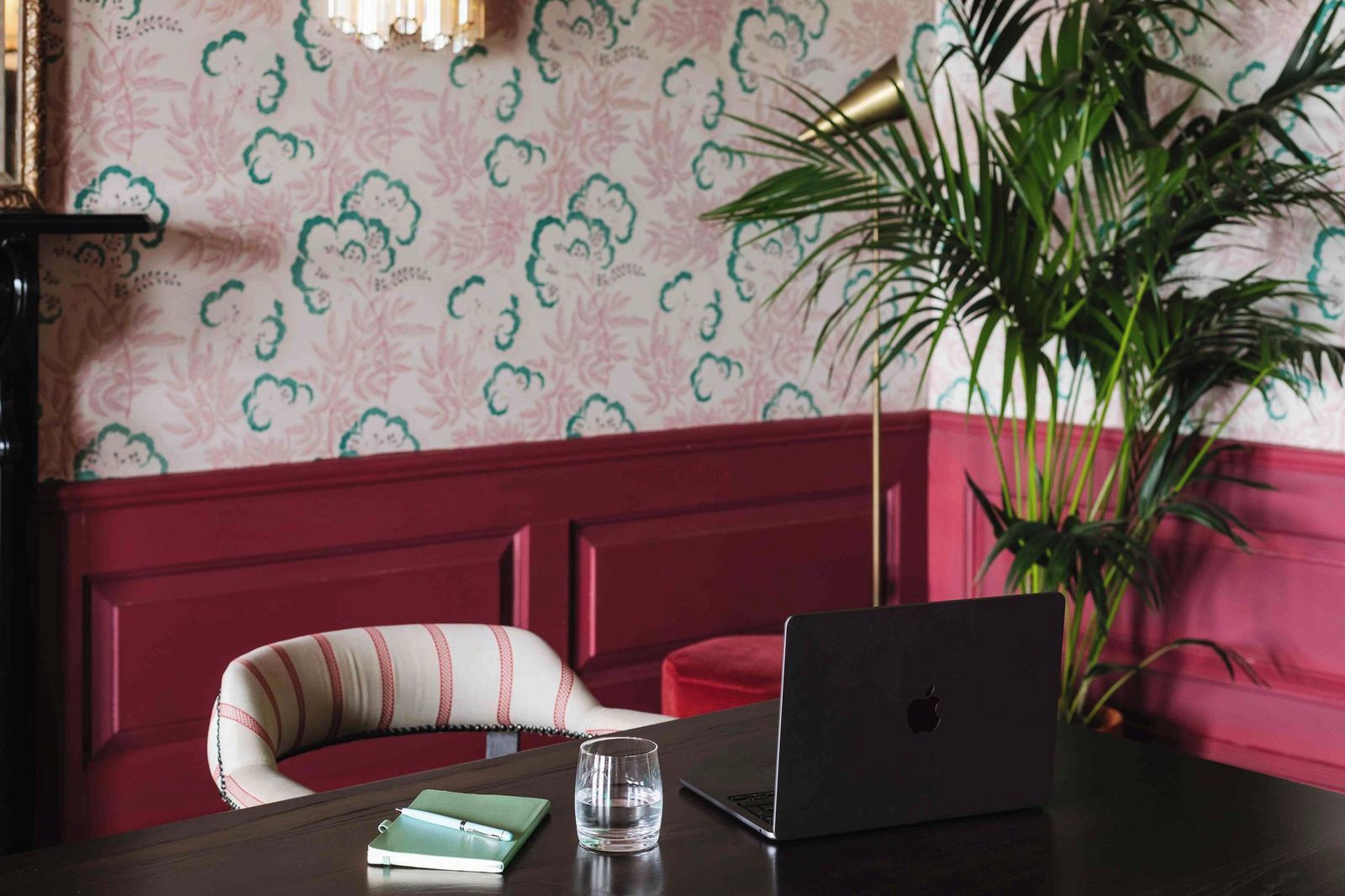 A room with a red bench, a laptop, a glass of water, a notebook, and a potted plant.