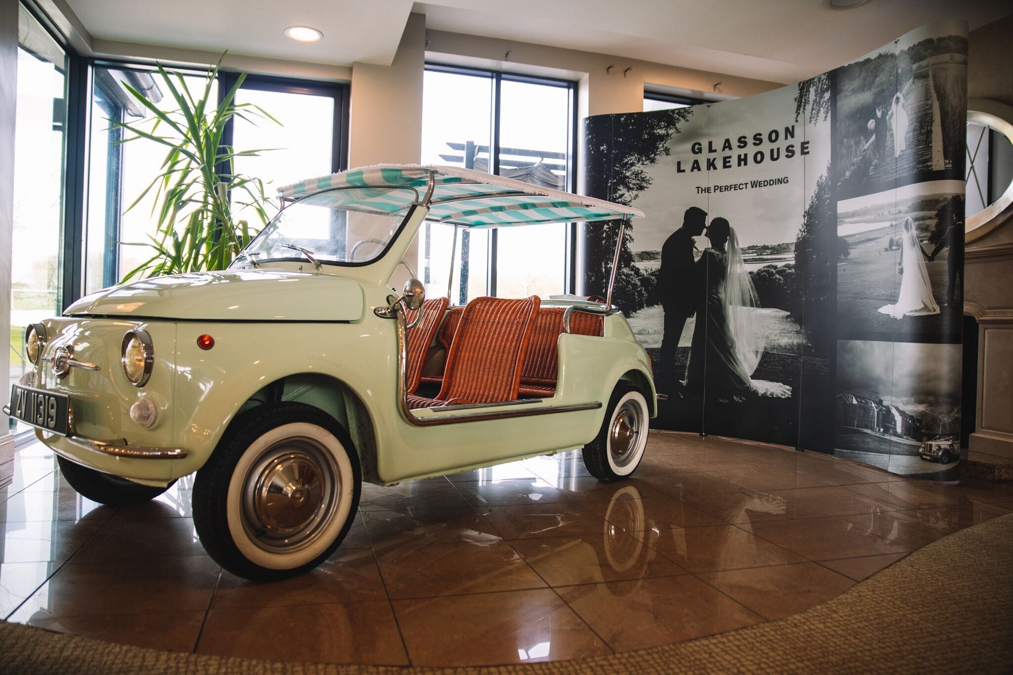Carro antigo com toldo xadrez em concessionária, com um grande pôster de casamento ao fundo.