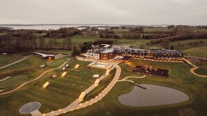 Un campo de golf con un club de campo, un estanque grande y una masa de agua al fondo.