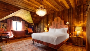 Un dormitorio acogedor con una cama grande, paredes de madera, una araña y un ventanal con cortinas.
