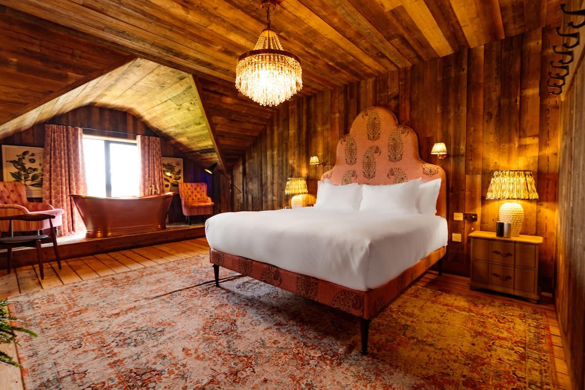 A cozy bedroom with a large bed, wooden walls, a chandelier, and a window with curtains.