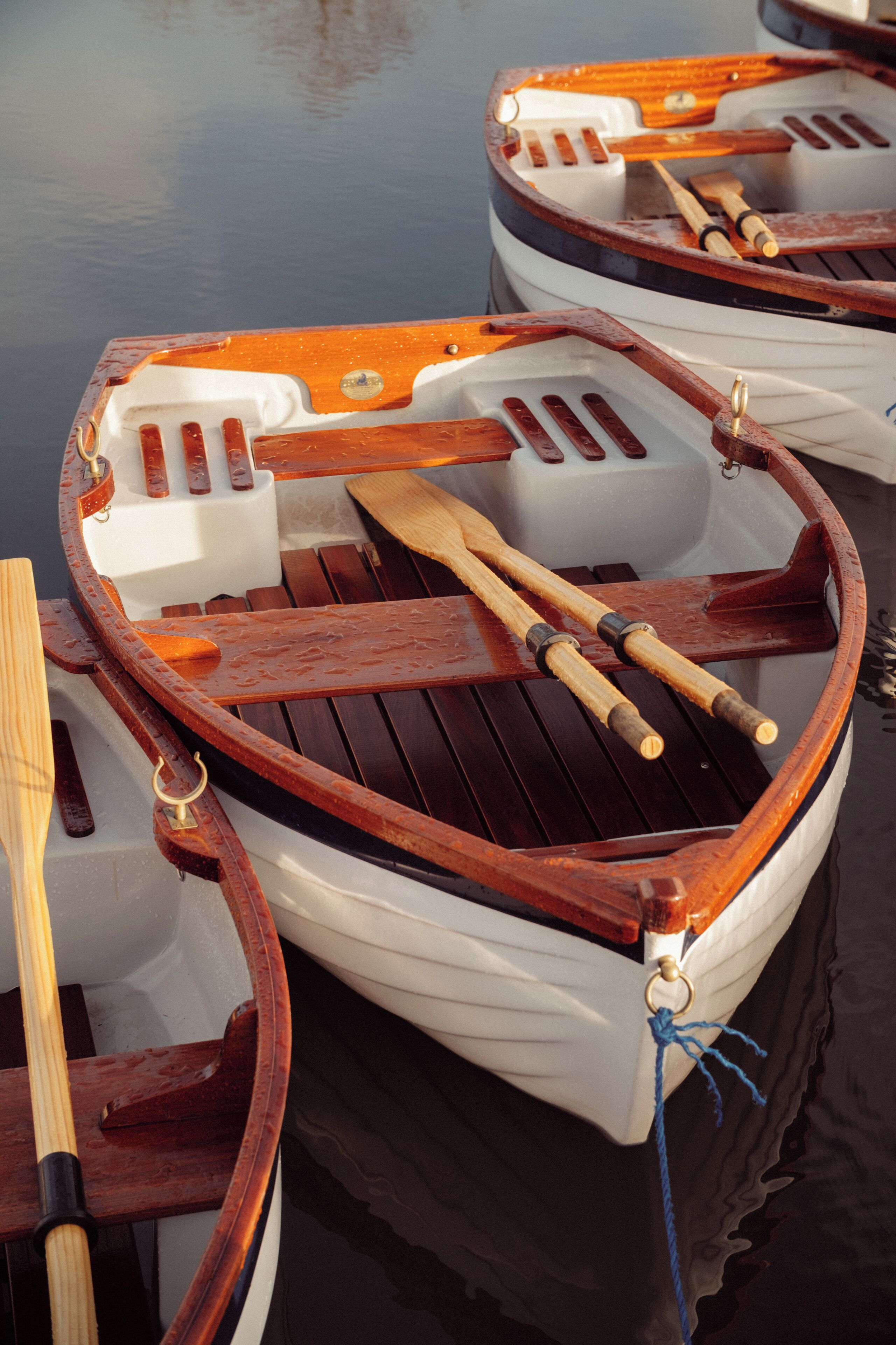 A rowboat with wooden oars and a white interior, tied to a dock.