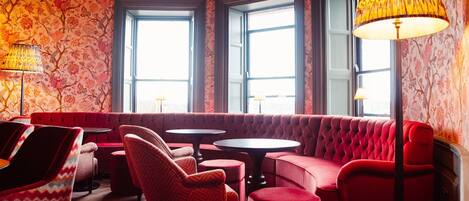 A room with a red upholstered sofa, two round tables, and a patterned wallpaper.