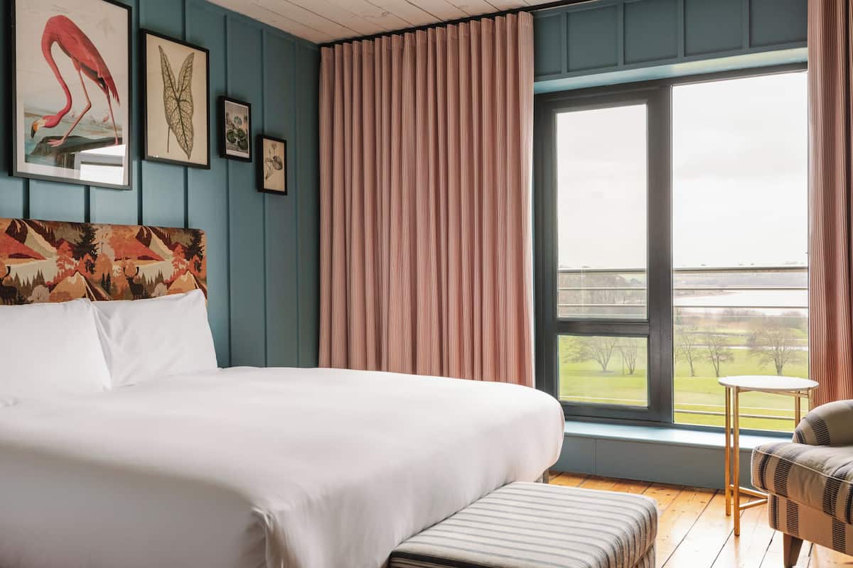 A bedroom with a large bed, a view of a green landscape through a window, and a chair by the window.