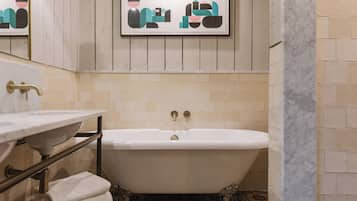 Un baño con bañera independiente, lavamanos con encimera de mármol y una obra de arte enmarcada sobre la bañera.